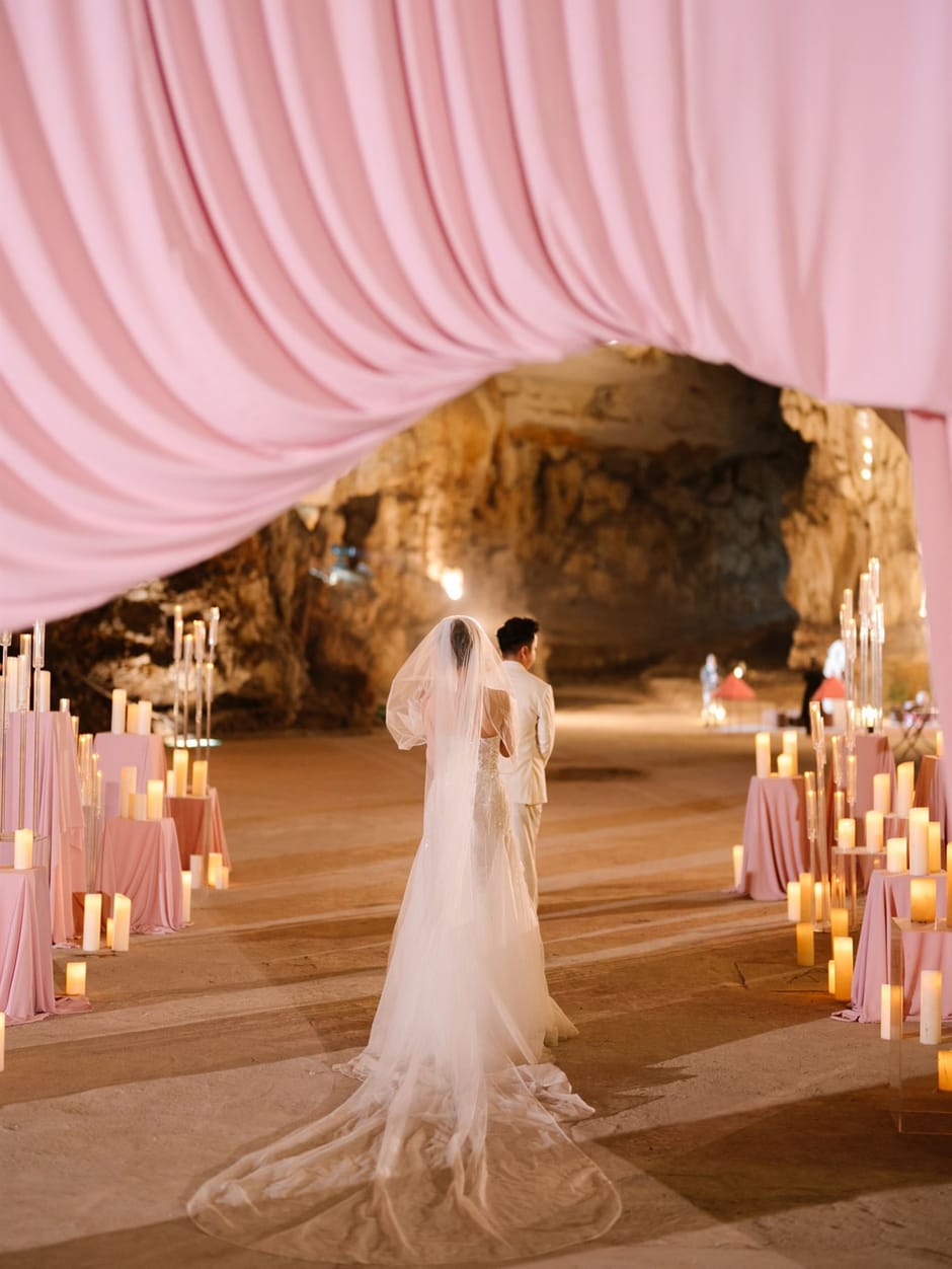 Bride and groom walking into a candlelit cave ceremony framed by pink drapery
