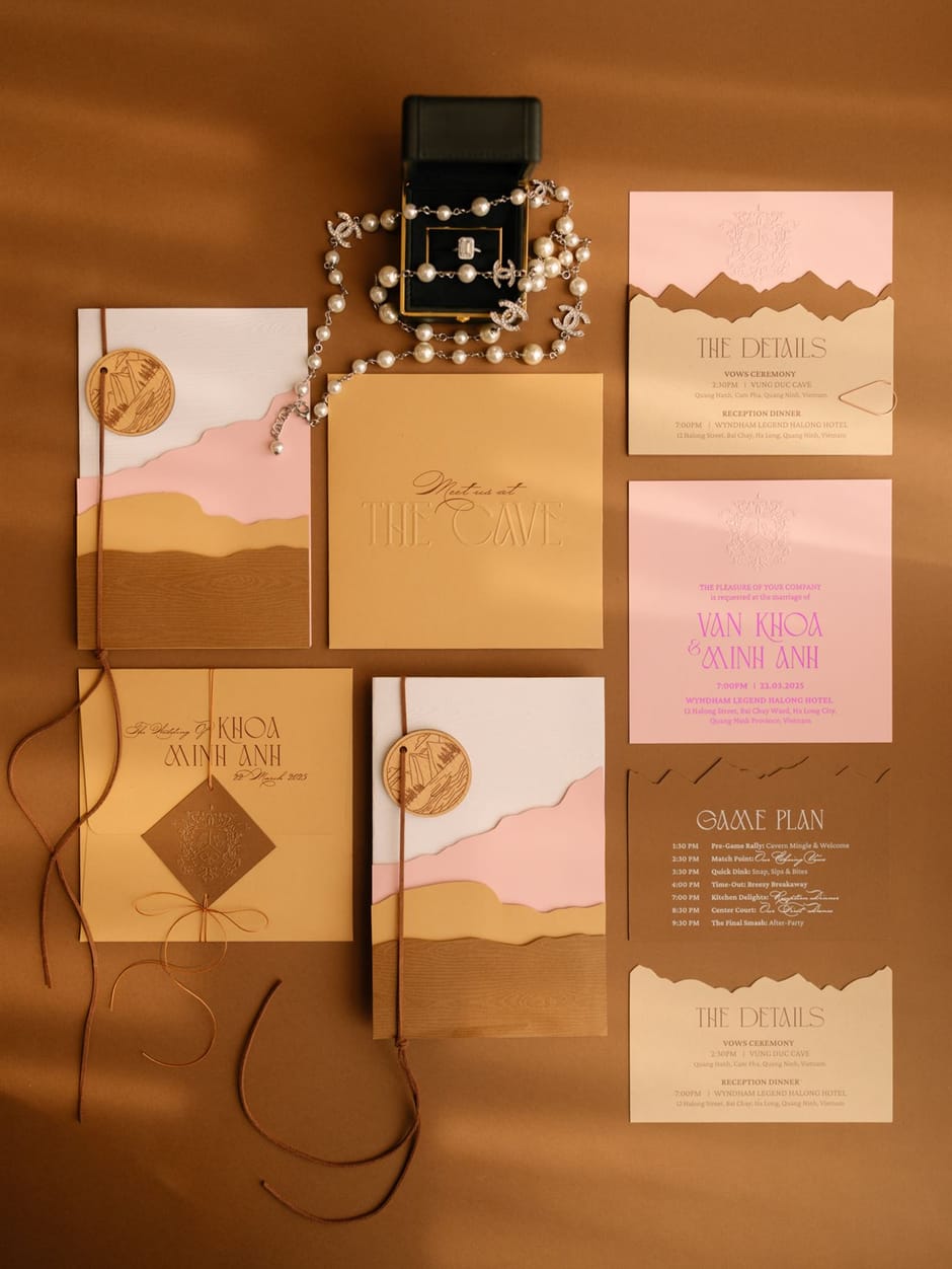 Flat lay of a desert-toned wedding invitation suite with pearl jewelry